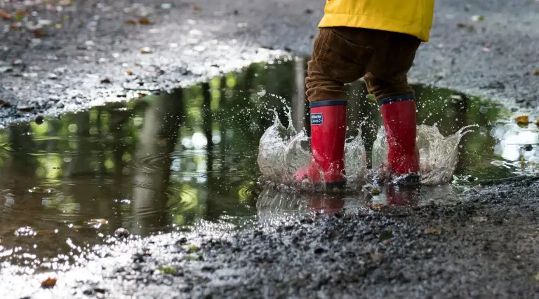 A toddler in wellies splashing in a puddle for outdoor learning in Scottish Primary Schools